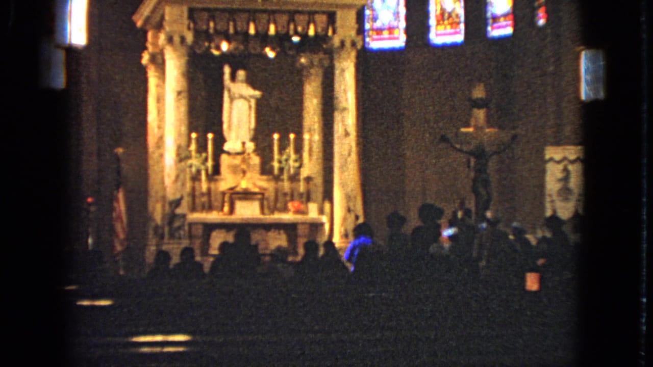 1963 Barrington church interior with a bright altar, white statue, side crucifix, colored stained glass, and a seated congregation in silhouette.
