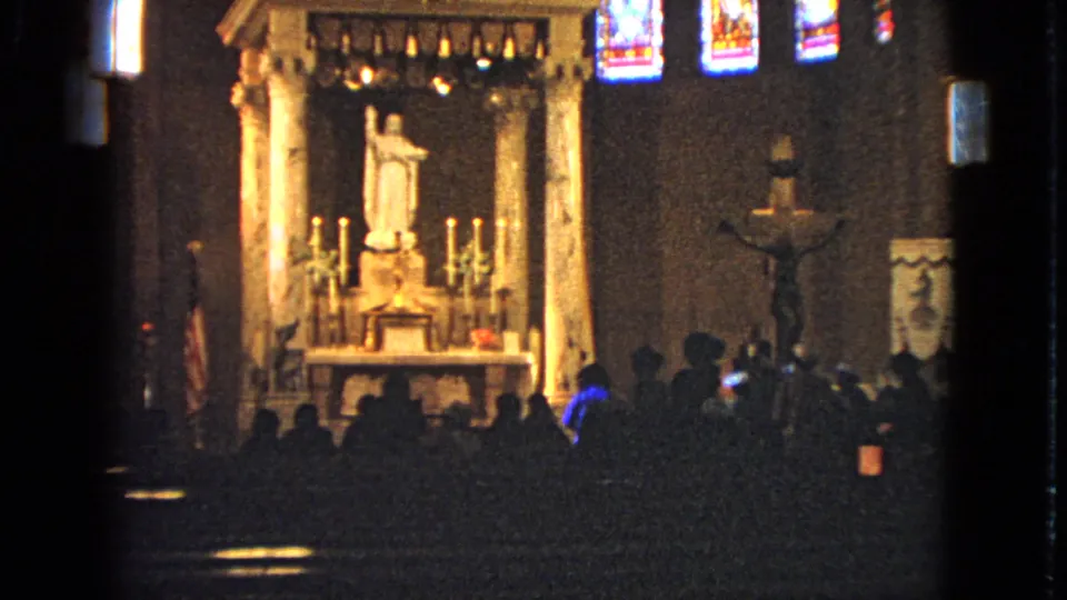 1963 Barrington church interior with a bright altar, white statue, side crucifix, colored stained glass, and a seated congregation in silhouette.