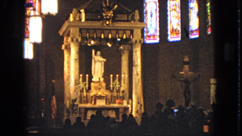 1963 Barrington church frame showing a formal altar area, white statue, crucifix, stained glass windows, and congregants seated in a dark nave.