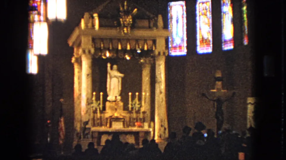 1963 Barrington, Illinois 8mm frame showing a Catholic church altar, statue, candles, stained glass, and worshippers silhouetted in the foreground.