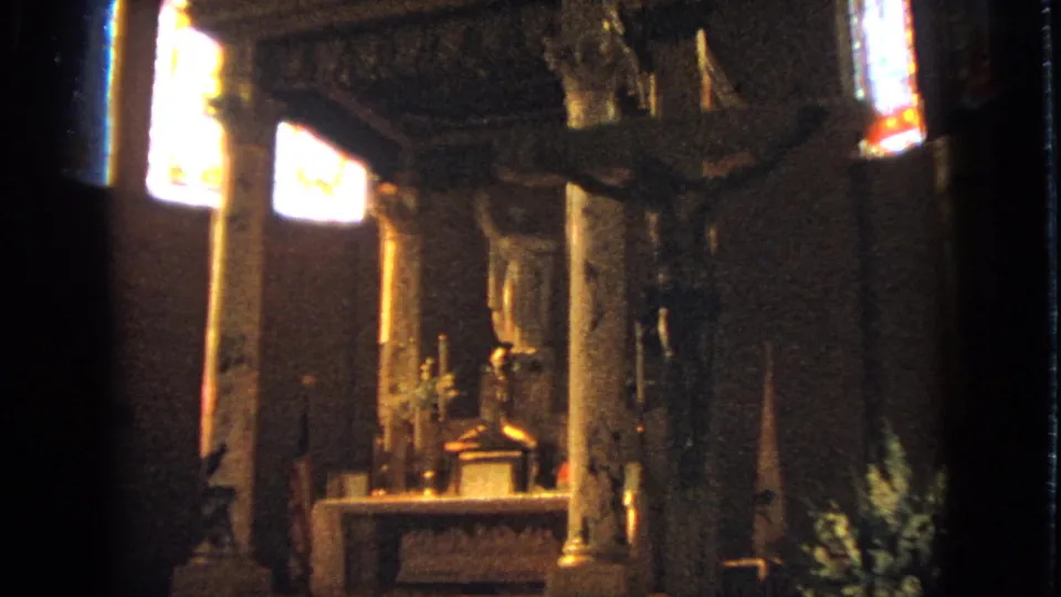 1963 Barrington, Illinois church interior seen from the side, with bright stained glass, an altar, candles, and religious sculpture in warm low light.