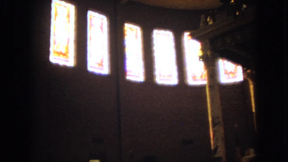 1963 Barrington, Illinois church interior frame looking toward a row of bright stained glass windows above the dark sanctuary wall.