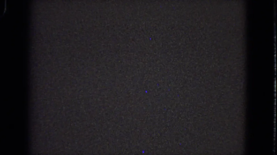 Final low-light 8mm frame from the 1963 Barrington stained-glass clip, showing grainy wall texture, dark borders, and sparse blue specks.