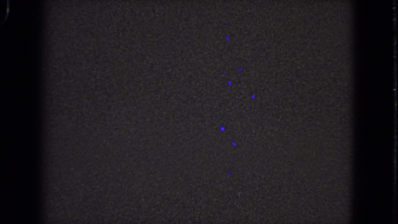 Dark underexposed 8mm frame with partial blue specks and film borders.