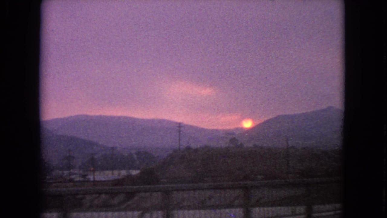 Sunset over dark hills with power lines and a roadside foreground.
