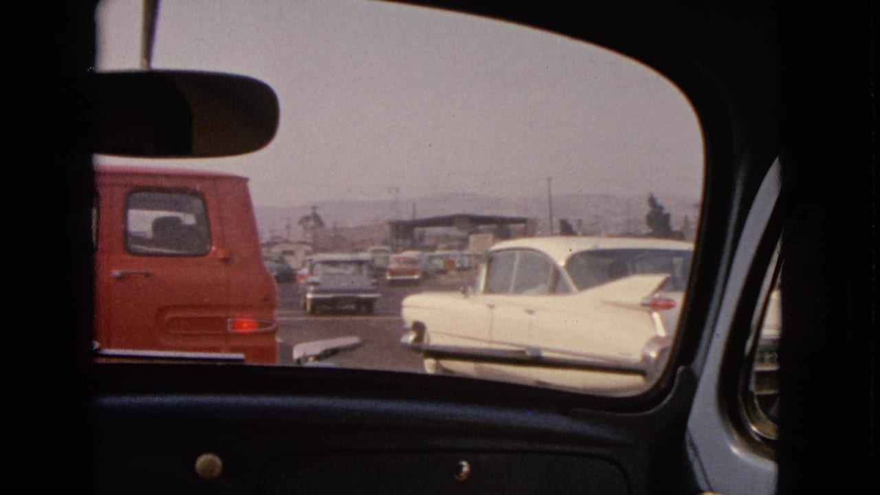 Rear-window view of traffic with a red van and white classic sedan on a roadway.