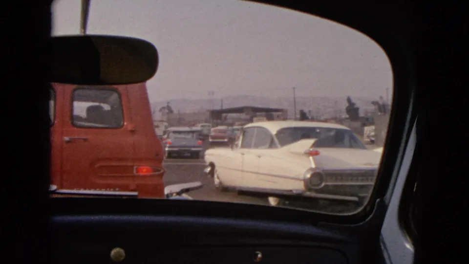 1963 Barrington, Illinois road scene framed by a car interior, showing a red van and white classic sedan in traffic.