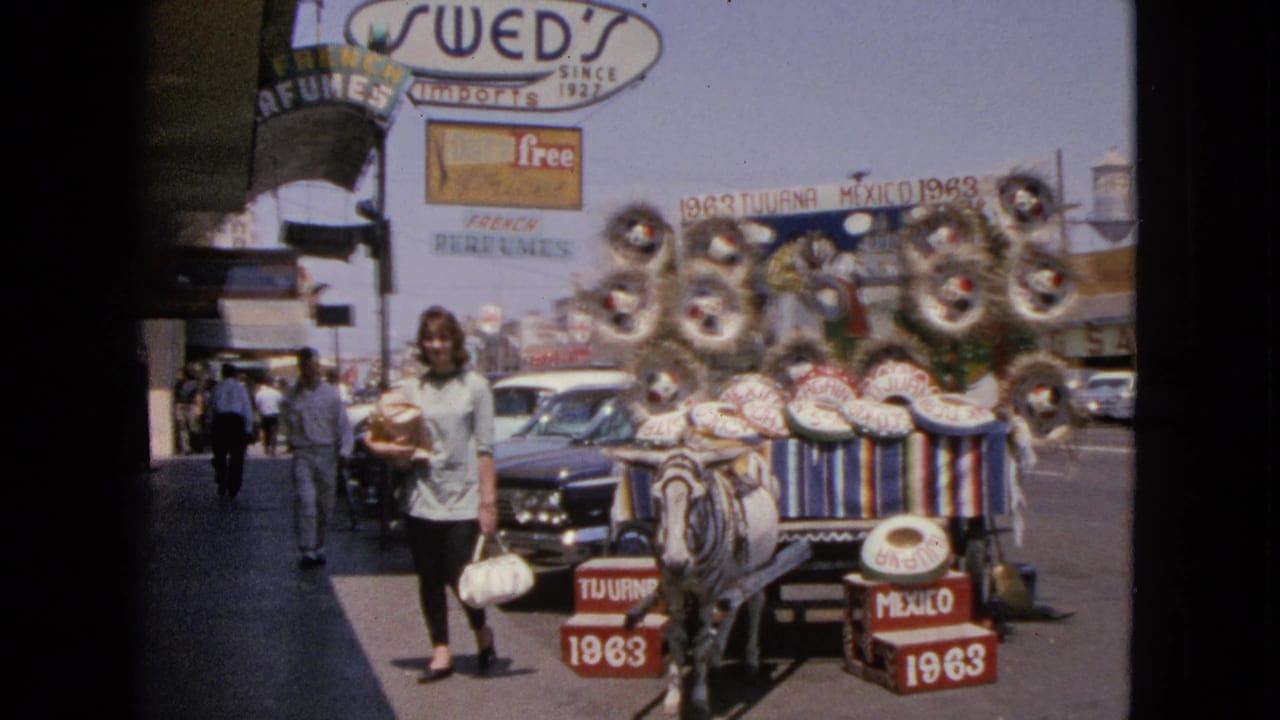 Woman walking near a donkey cart display with sombreros, red crates, storefront signage, and cars behind her.