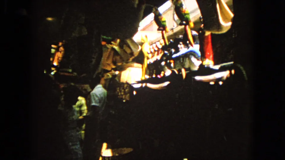 Barrington 1963 home-movie frame showing adults near illuminated gaming or amusement equipment in a dark interior.