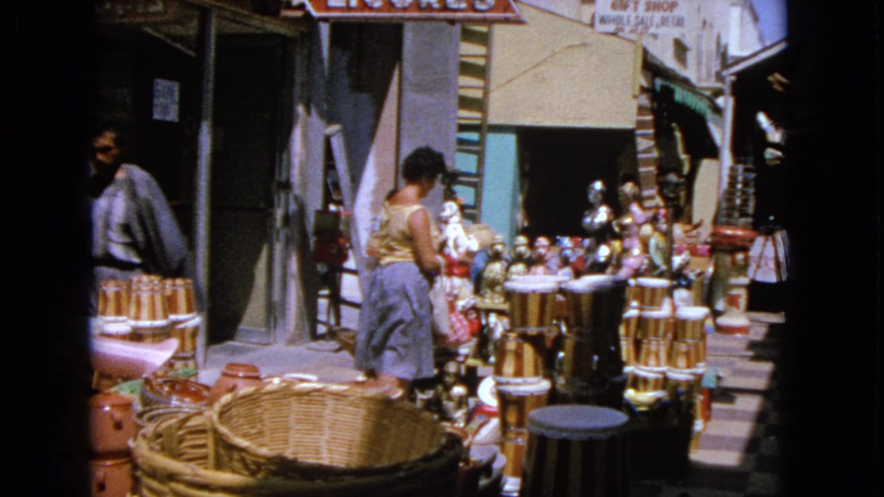 Woman in a yellow top browses outdoor market goods beside baskets and ceramic jars.