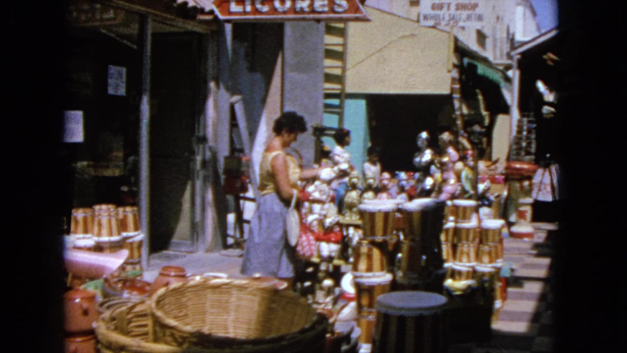 Woman stands beside display tables of pottery, baskets, and figurines outside a shop.