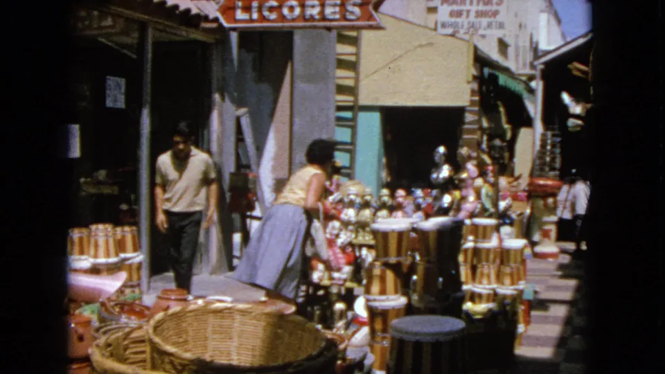 At the end of the clip, the woman leans into the outdoor display while a man remains near the shaded entrance and signs hang above.