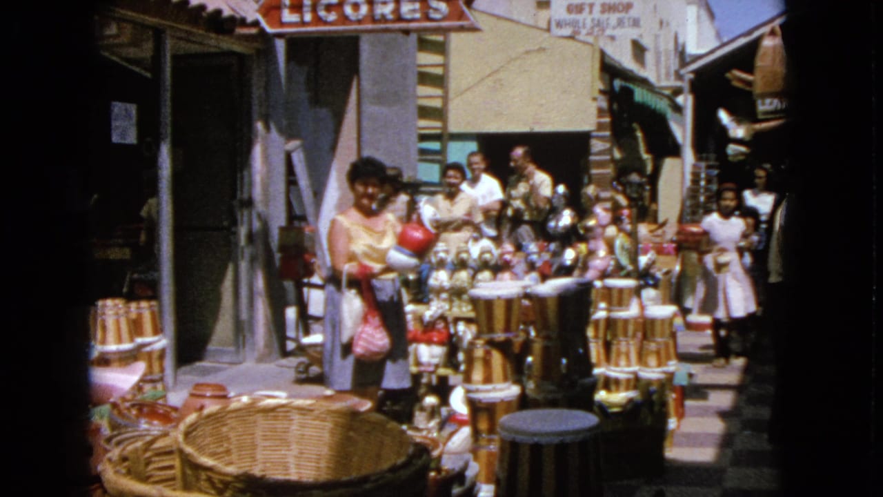 Shoppers browse baskets and goods outside storefronts with LICORES and GIFT SHOP signs.