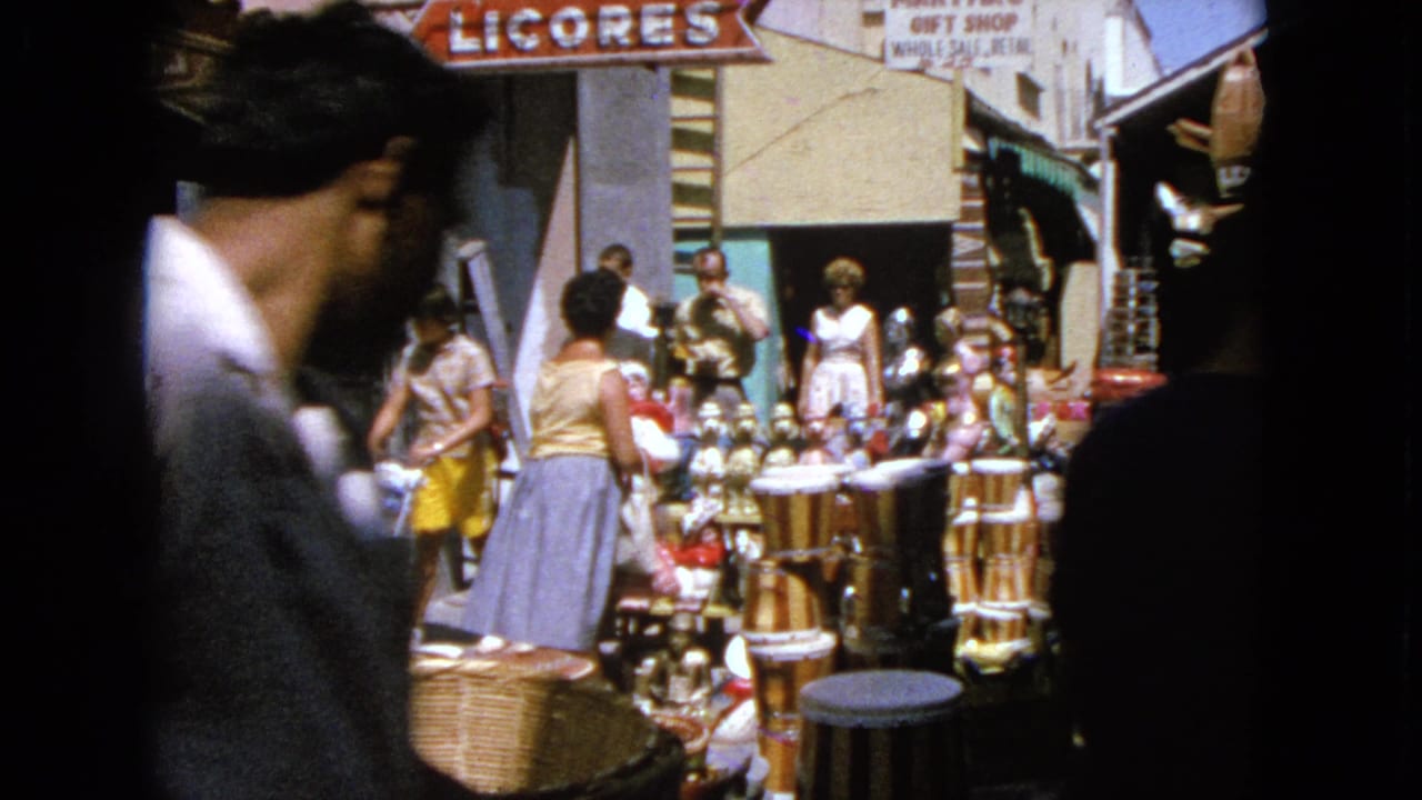 A man passes close to the camera as shoppers stand near baskets and shop displays.