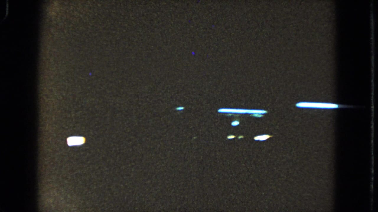 Dark grainy frame with bright horizontal light streaks and black film borders.