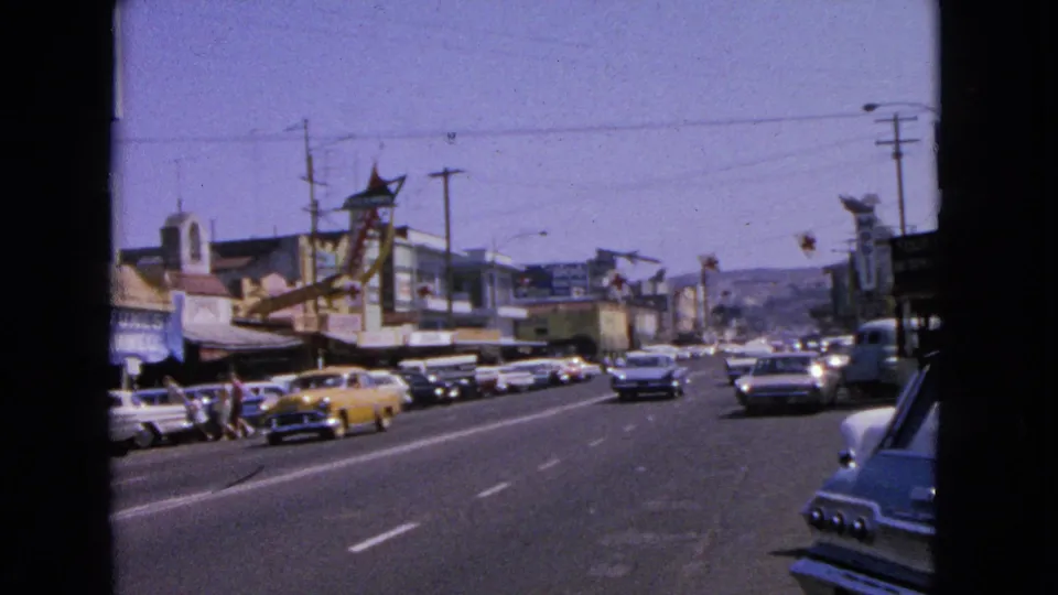 1963 Barrington street view with parked classic cars, retail buildings, overhead wires, signs, and traffic moving through the frame.