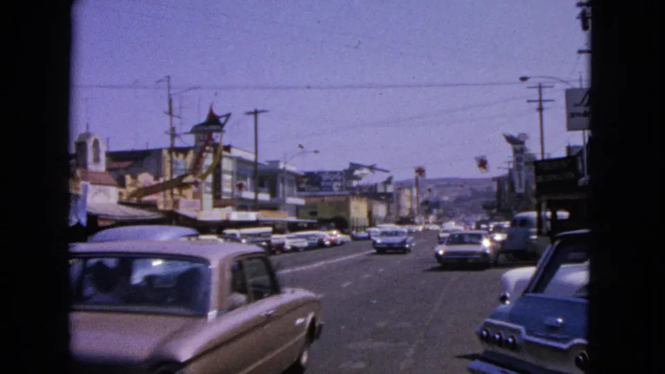 1963 Barrington, Illinois street view with early-1960s cars moving past storefronts, utility poles, and dark 8mm frame edges.