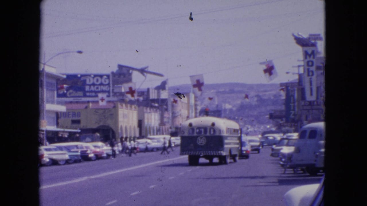 1963 Barrington, Illinois street view with a bus marked 16, classic cars, overhead cross flags, storefronts, and visible Mobil and dog racing signage.