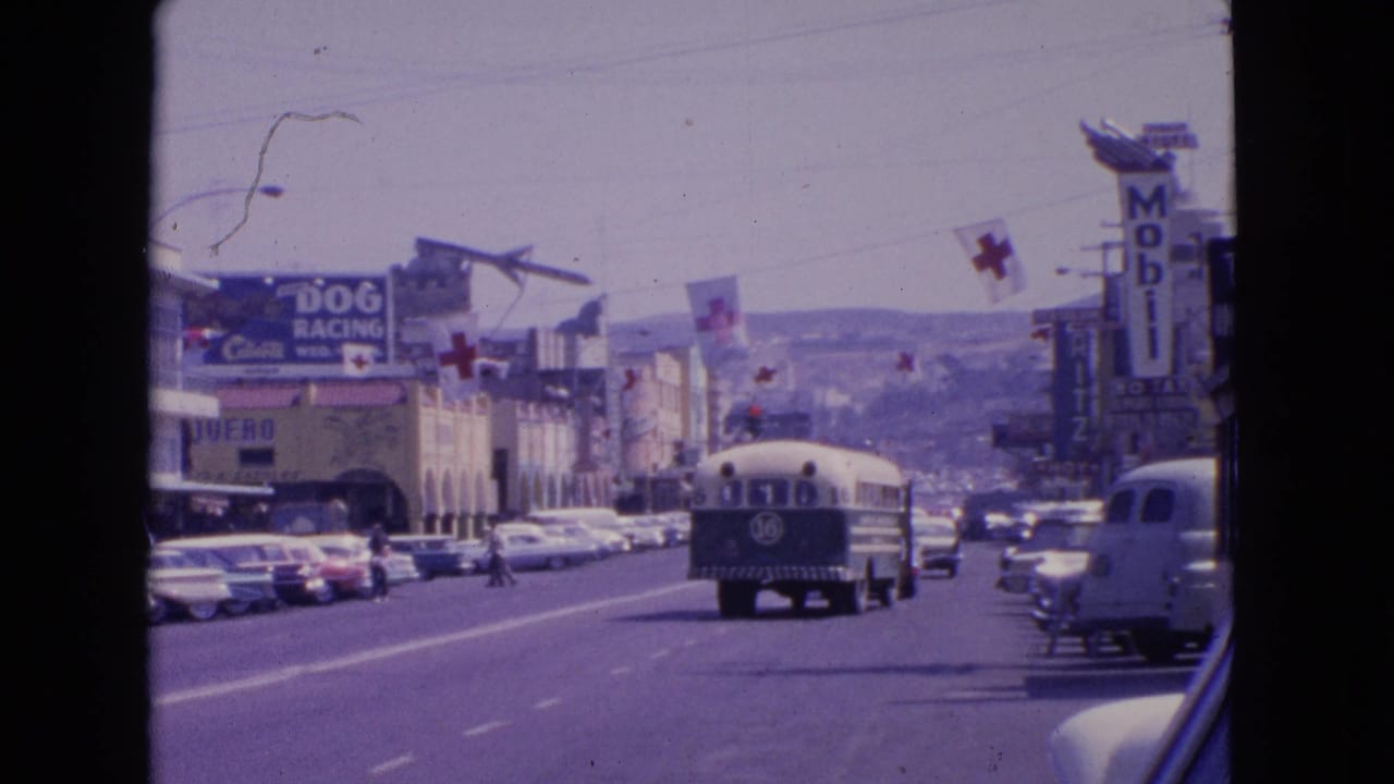 1963 Barrington, Illinois street scene with a bus, parked cars, pedestrians, overhead cross flags, and commercial signs including Mobil and dog racing.