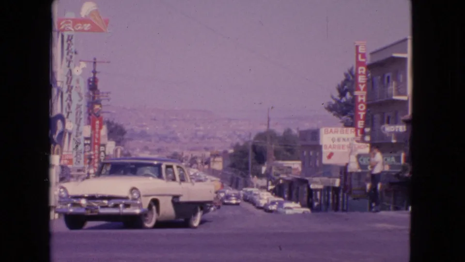 The white sedan continues through the Barrington street scene, with classic cars, storefront signs, and distant hills visible.