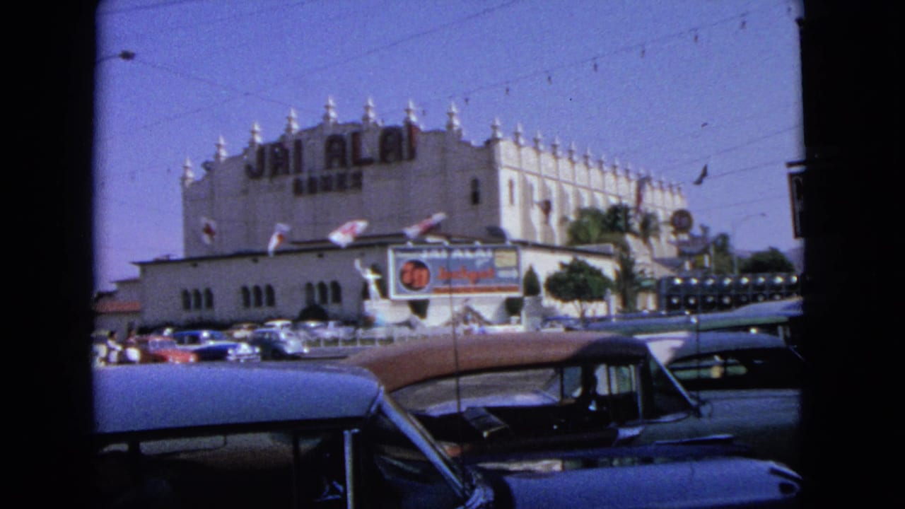 1963 home-movie frame showing traffic at an intersection before a large Jai Alai building with signage and palm trees.