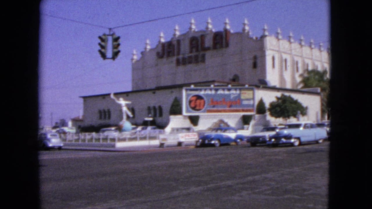1963 street view with early-1960s cars, a traffic signal, palm trees, and a Jai Alai building exterior.