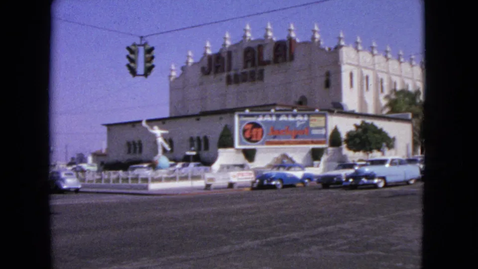 1963 street view with early-1960s cars, a traffic signal, palm trees, and a Jai Alai building exterior.