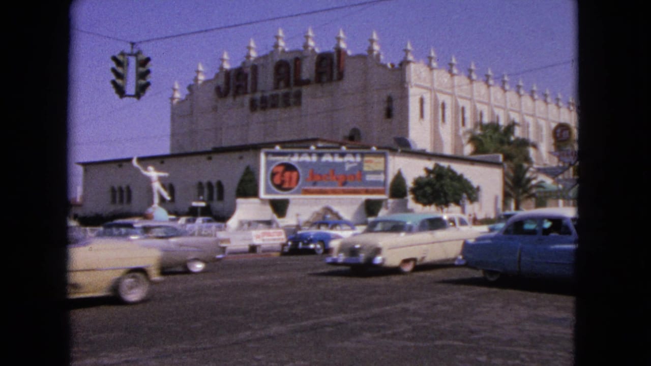 Street view with classic cars passing the Jai Alai building and roadside signage.