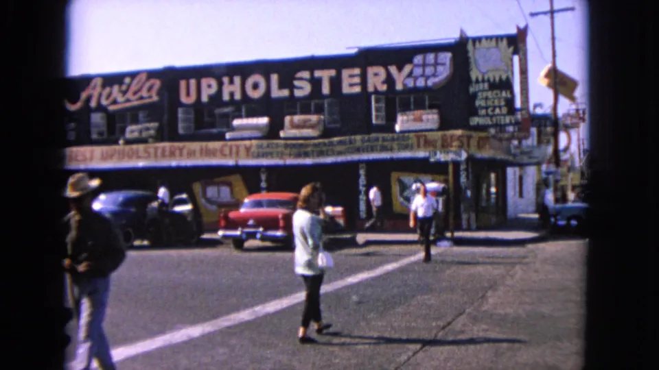 In Barrington, Illinois, a woman pauses near a crosswalk while pedestrians and classic cars appear outside Avila Upholstery.