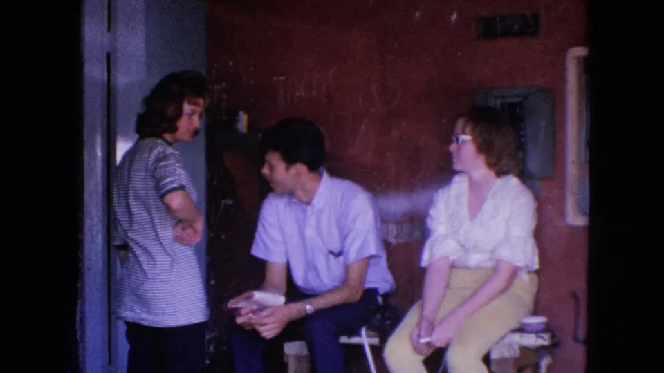 Barrington, Illinois 1963 frame showing a standing adult speaking with a seated man beside a woman in white sunglasses.