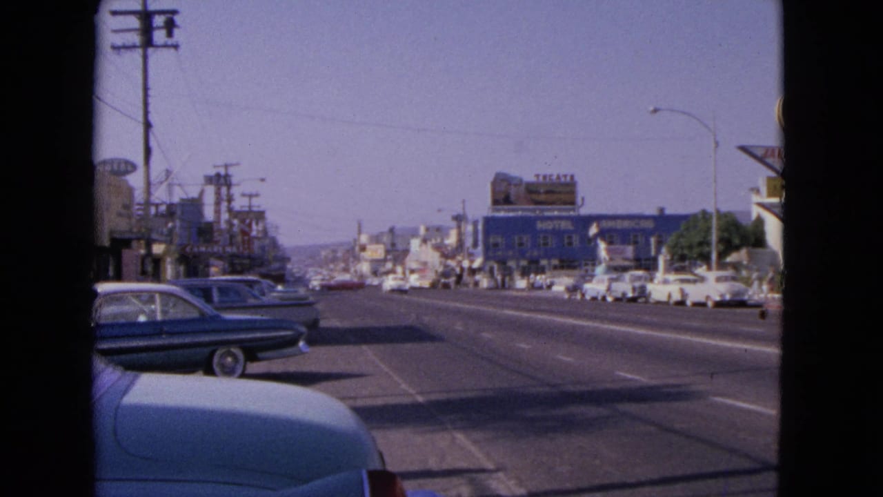 1963 Barrington, Illinois street view with classic cars along a broad road, storefront signs, utility poles, and visible 8mm frame edges.