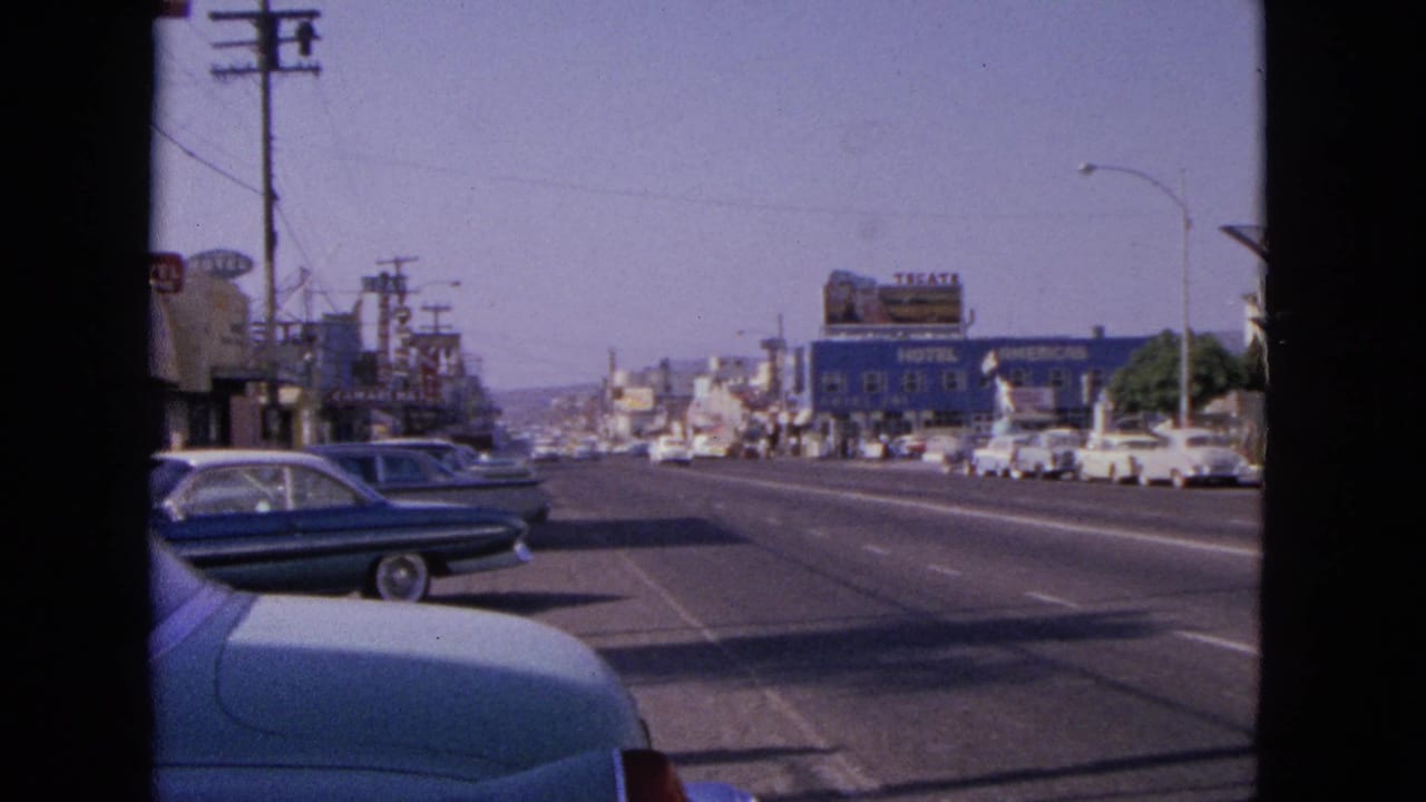 Street scene with blue and white cars, utility poles, low buildings, and storefront signage.