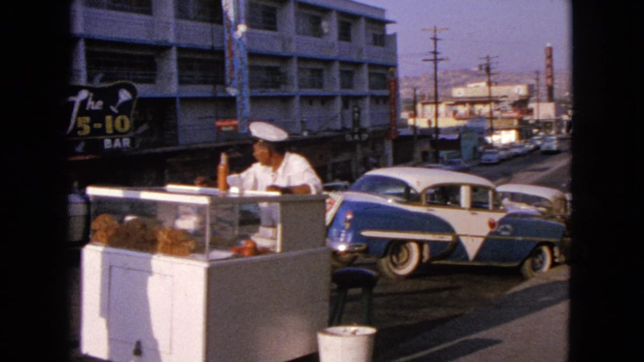 1963 Barrington street view with a vendor at a white hot dog stand, a blue-and-white 1950s sedan, storefronts, and bar signage.