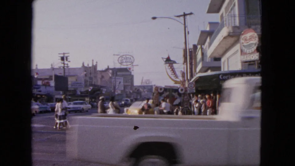 A passing car partially obscures pedestrians near storefronts and visible signs in the 1963 Barrington street scene.