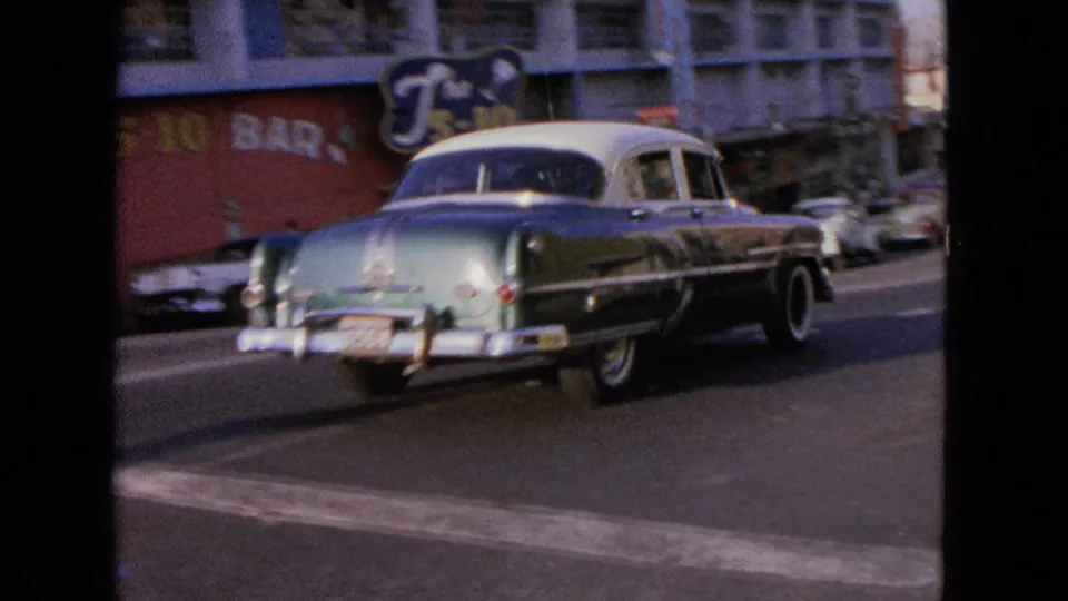 Blue and white mid-century sedan traveling along a commercial street in the supplied 1963 Barrington, Illinois home-movie footage.