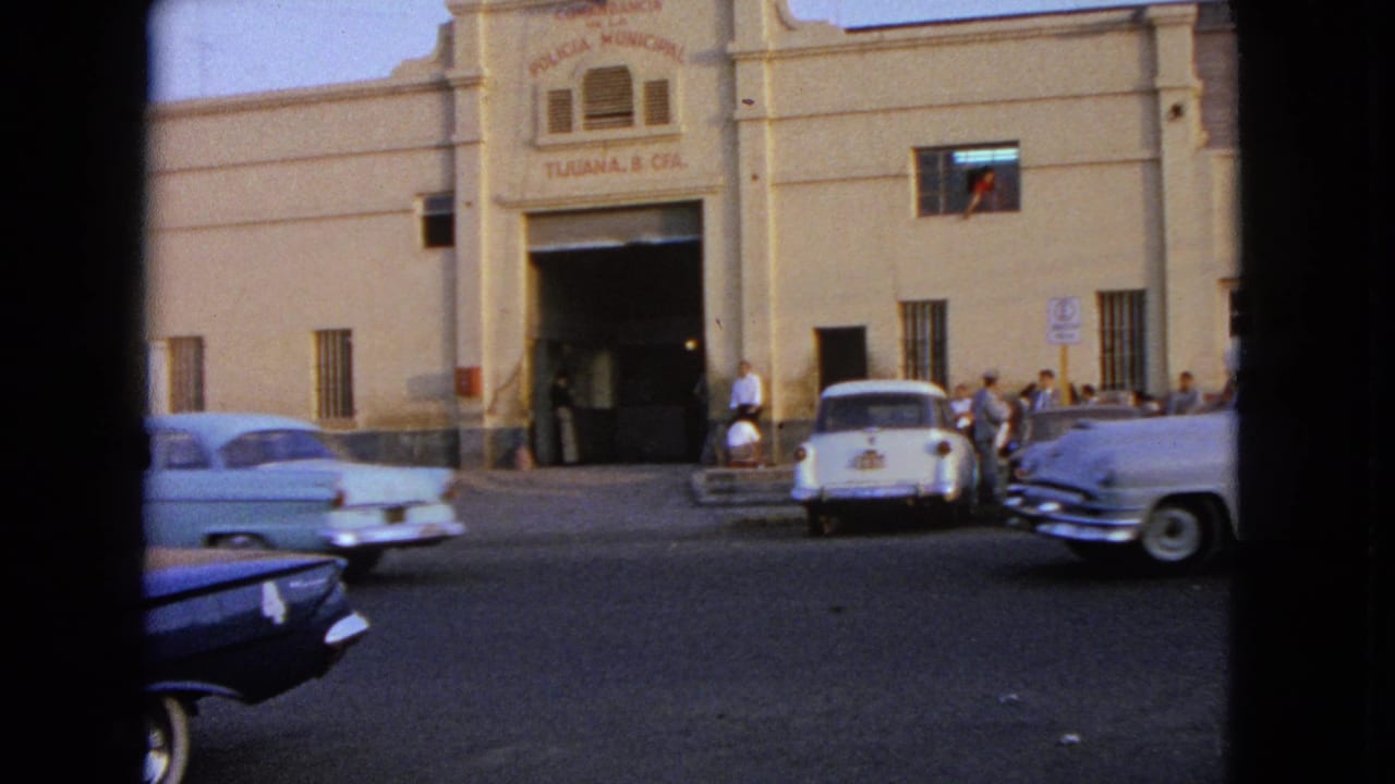Street view of parked and moving classic cars outside a municipal facade.