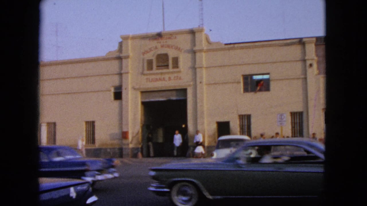 Street view of a beige building with cars passing and pedestrians near the entrance.