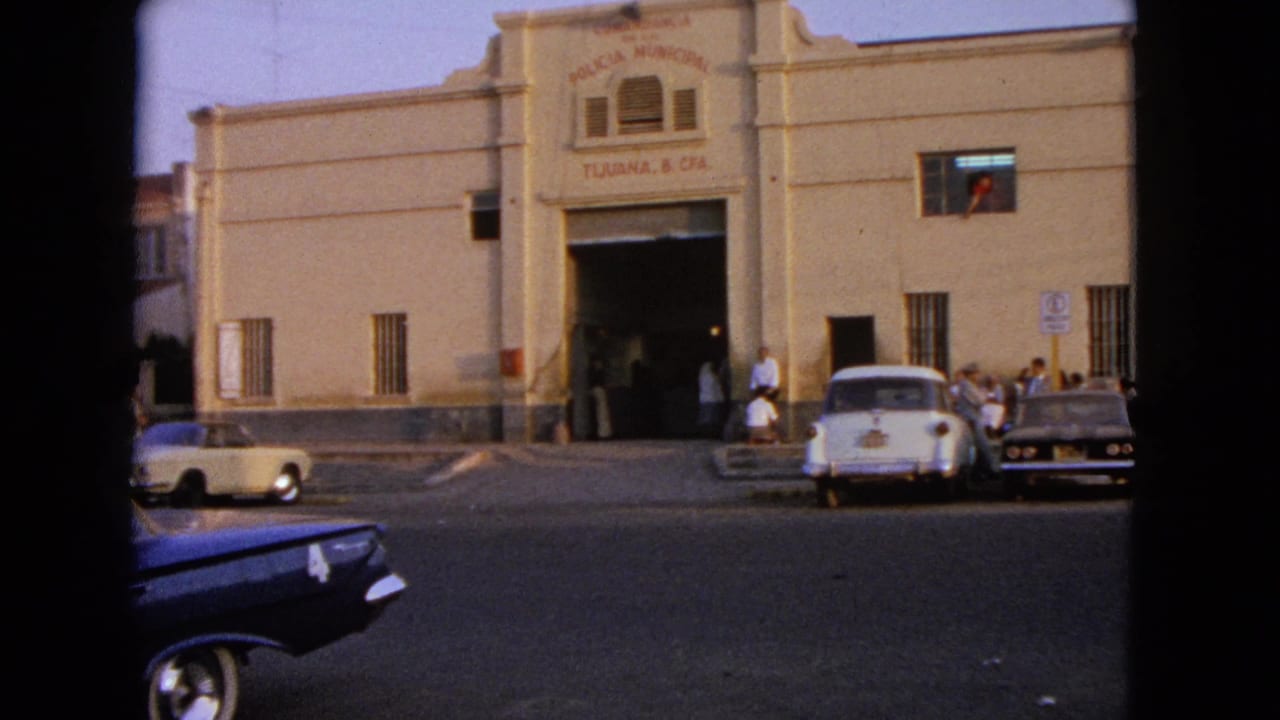 Municipal-looking building with parked cars, pedestrians, and a car moving through the foreground.