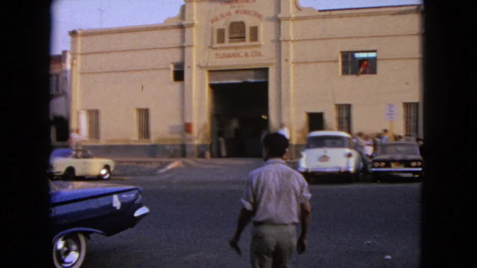 A man in a light shirt crosses toward the entrance of a building signed Policia Municipal and Tijuana, B. C., Mx., with cars nearby.