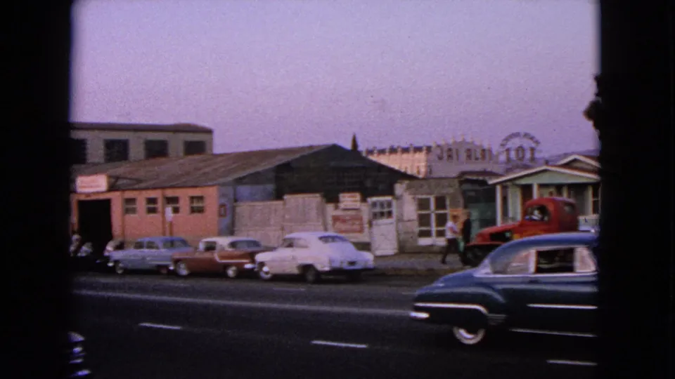 1963 Barrington street view with rows of parked classic cars, low roadside buildings, and a red tow truck near the curb.