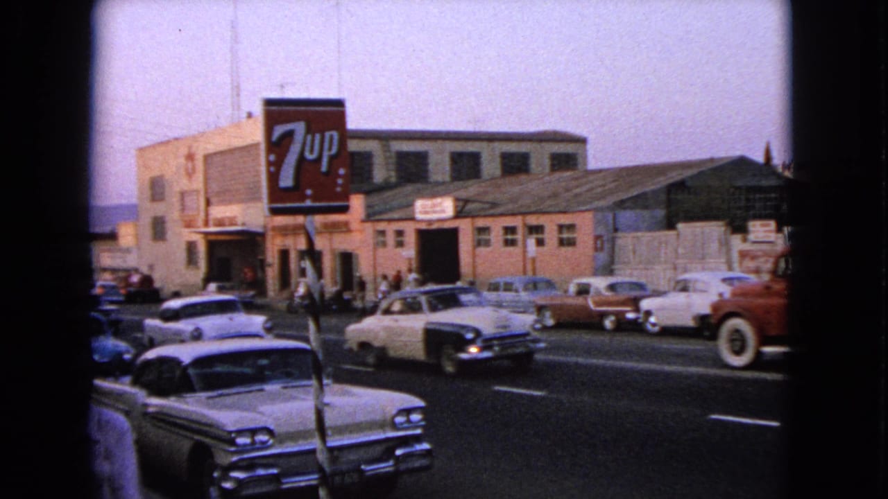 Barrington, Illinois street traffic in 1963, with mid-century cars passing a prominent 7-Up sign and pedestrians near the sidewalk.