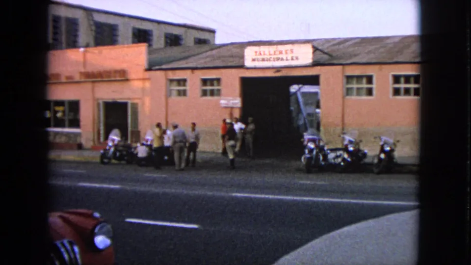 Barrington, Illinois 1963 street view with pedestrians, motorcycles, and a pink building bearing the sign “TALLERES MUNICIPALES.”