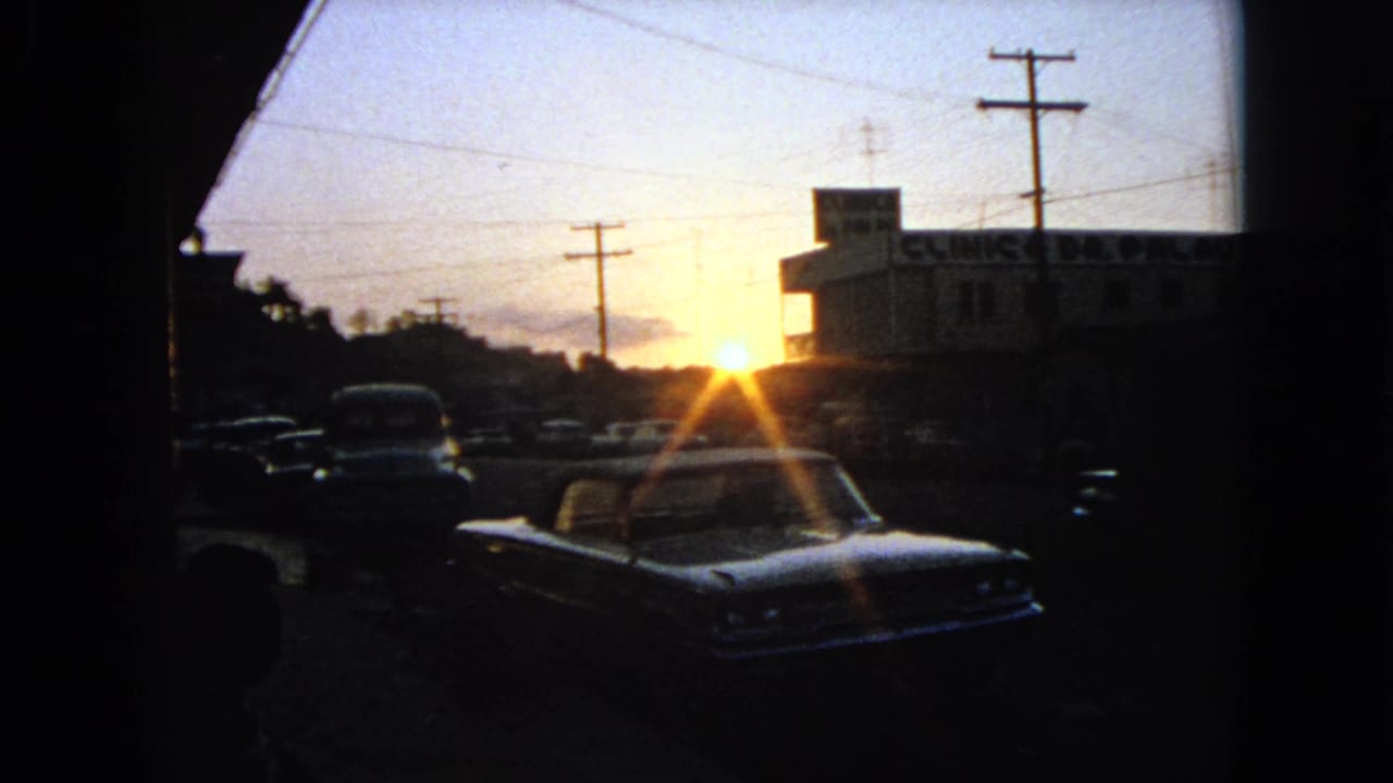 1963 Barrington, Illinois parking lot view with a foreground car silhouetted against sunset near a clinic building and utility poles.