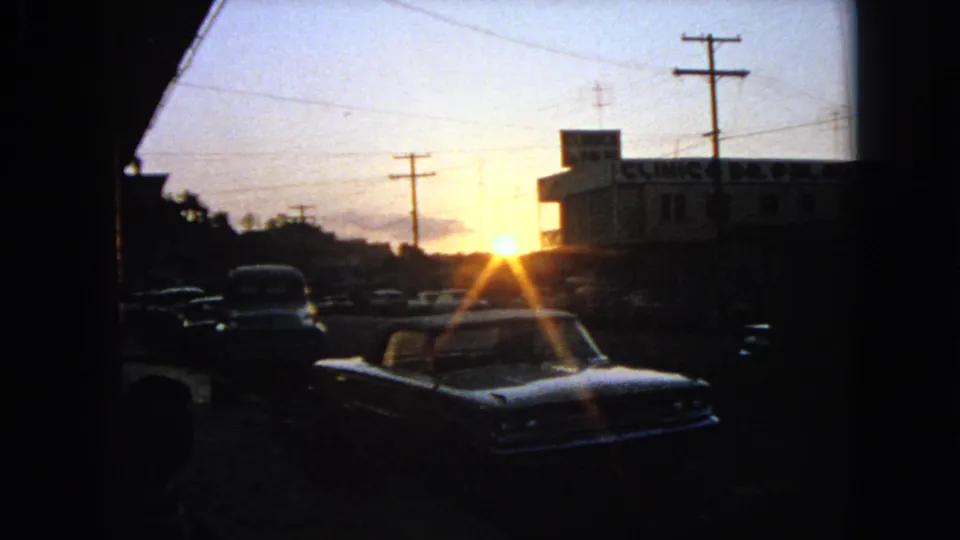 1963 Barrington, Illinois parking lot view with a foreground car silhouetted against sunset near a clinic building and utility poles.