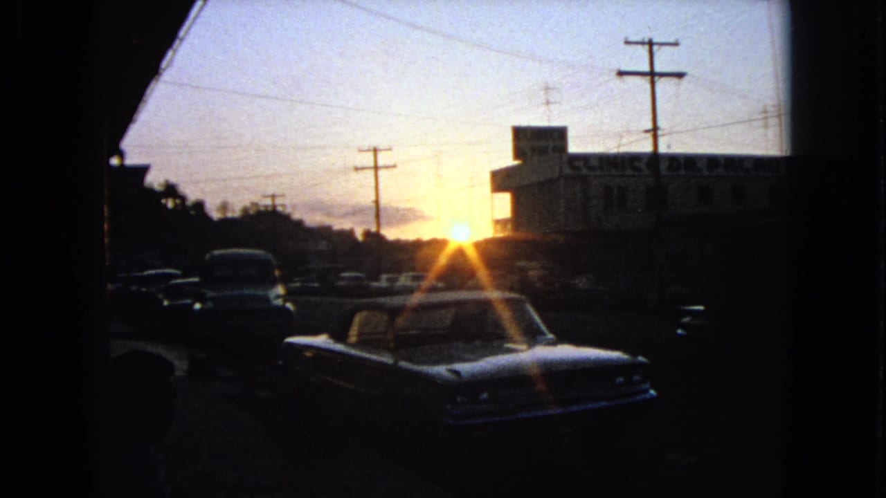 1963 Barrington, Illinois dusk frame showing parked cars, a clinic exterior, overhead wires, and strong sun flare.
