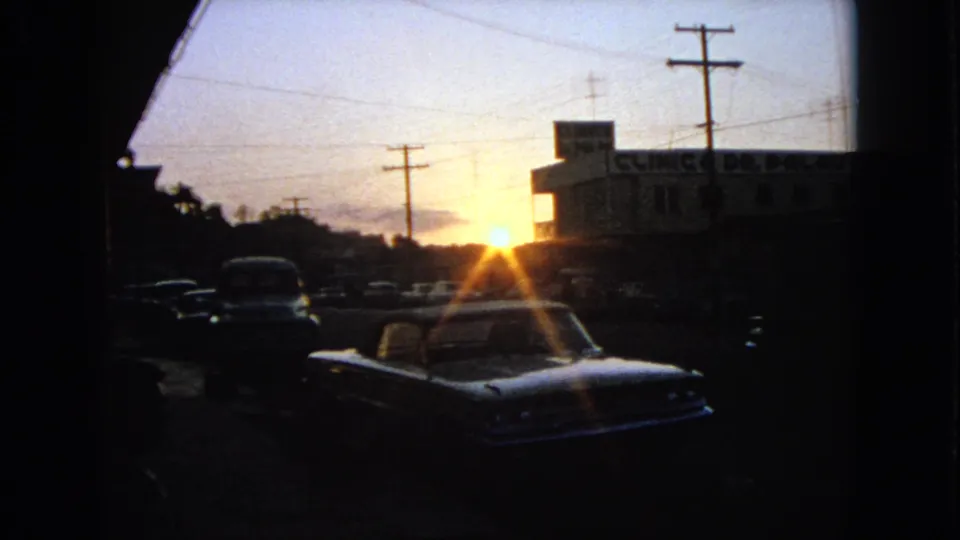1963 Barrington, Illinois parking-lot frame with vintage cars in deep shadow and a clinic building near the sunset.