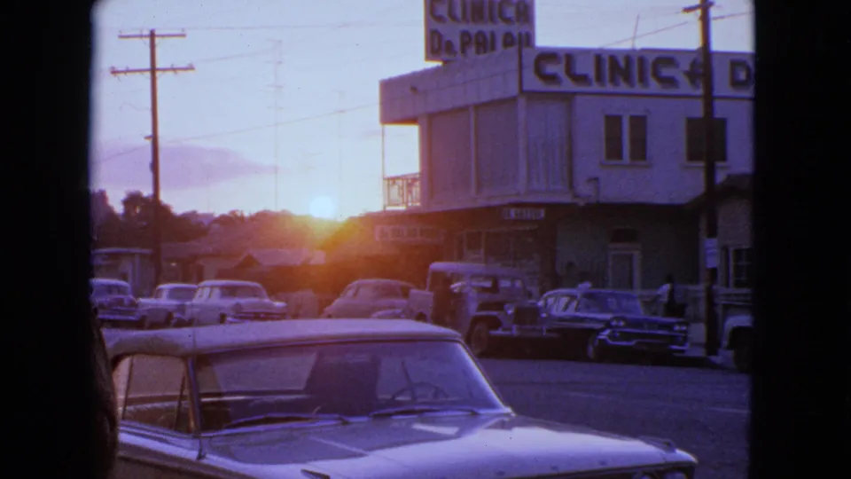A clear final view of the Barrington street shows parked mid-century cars, clinic signage, utility poles, and strong sunset flare.