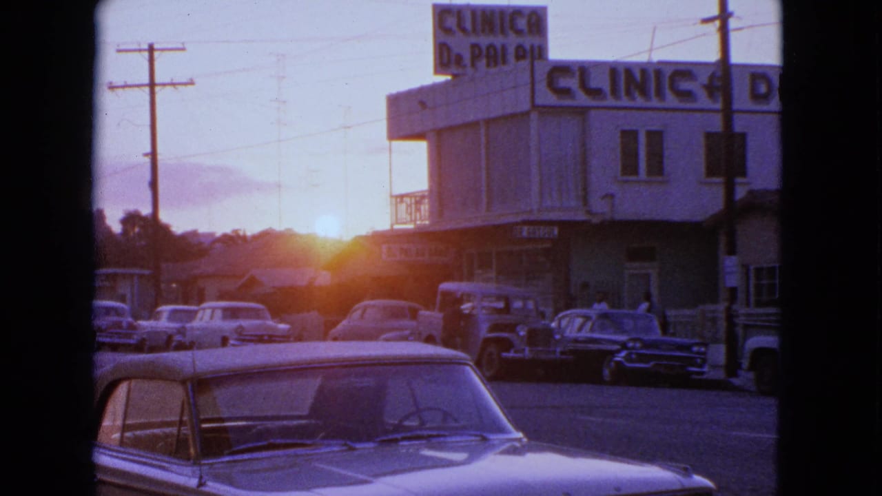 1963 Barrington, Illinois street view with parked cars, overhead wires, and a building marked with a clinic sign in warm sunset light.