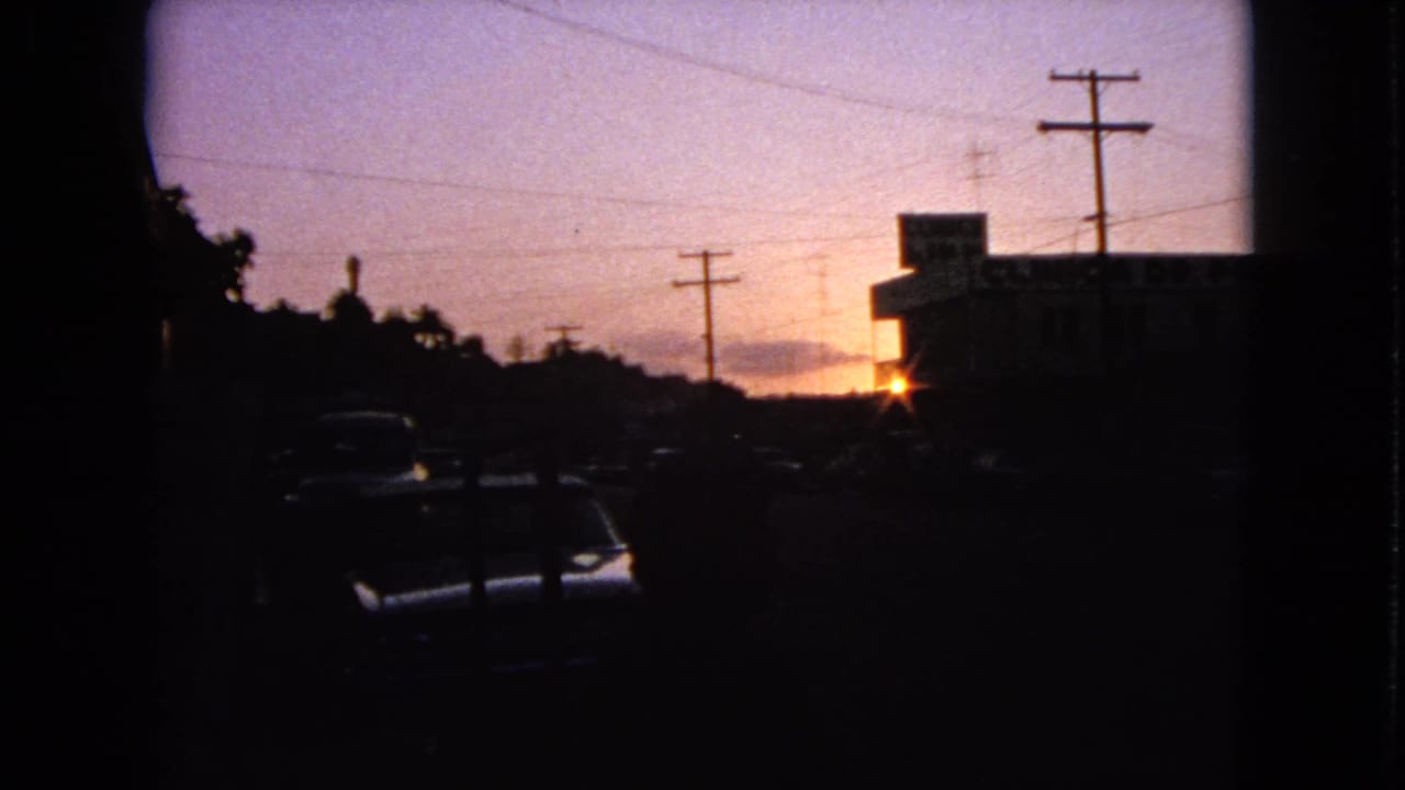 A dusk street view in Barrington, Illinois, with parked cars in shadow, utility poles, and a low building silhouetted by the setting sun.