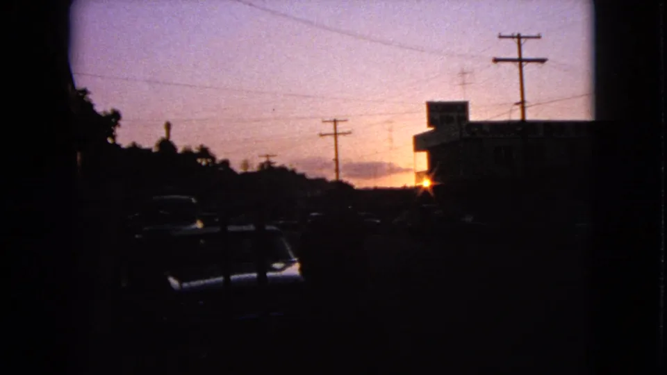 A dusk street view in Barrington, Illinois, with parked cars in shadow, utility poles, and a low building silhouetted by the setting sun.